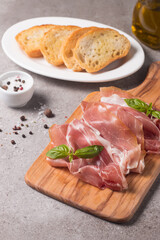 Closeup of thin slices of prosciutto with mixed olives and paprika on wooden cutting board