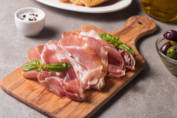 Closeup of thin slices of prosciutto with mixed olives and paprika on wooden cutting board