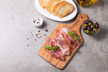 Closeup of thin slices of prosciutto with mixed olives and paprika on wooden cutting board