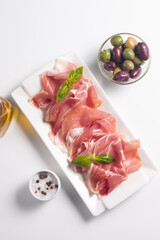Closeup of thin slices of prosciutto with mixed olives and paprika on wooden cutting board