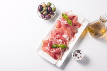Closeup of thin slices of prosciutto with mixed olives and paprika on wooden cutting board