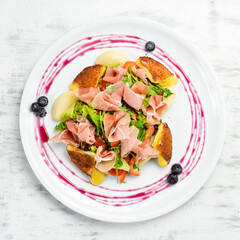 Prosciutto salad, brie cheese and vegetables on a white plate. Top view. Rustic style.