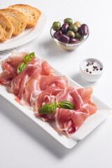 Closeup of thin slices of prosciutto with mixed olives and paprika on wooden cutting board
