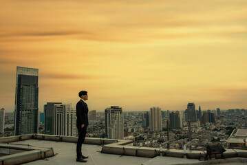 Asian business man in a suit standing and looking at the city view, confident and confident, successful in business, the sunset sky