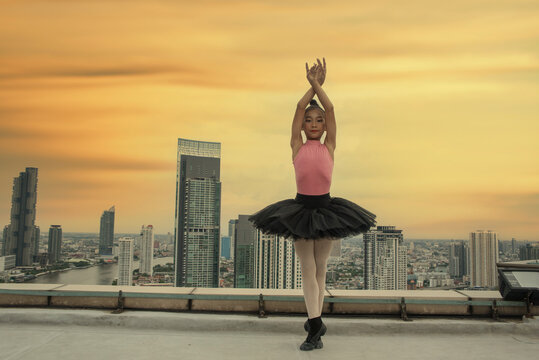 Asian girl in a ballet costume dances ballet on the rooftop of a high-rise building.  - Powered by Adobe