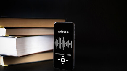 Audio listen book. Phone screen with audiobook app on paper books black background. Online education course, E learning class and e book digital technology concept.