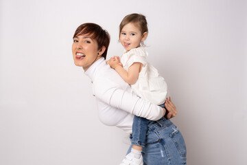 Photo of pretty young mommy hugging little daughter standing isolated over white background. Motherhood concept.