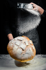 Fragrant white baked bread in women's hands. Black flour baking background.