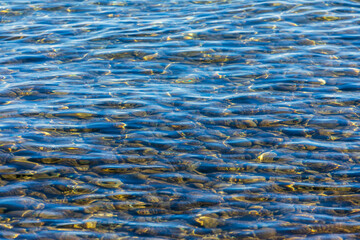Water background abstract, calm transparent water waves, trendy abstract nature background. Sunlight. Blurred of sea blue water surface which has stone background below.