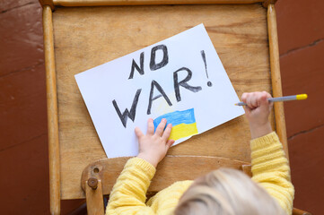 Ukrainian girl kid protesting against war conflict and drawing message text No War with Ukrainian flag on the white paper. No war, stop war, russian aggression, crisis, peace
