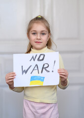 Ukrainian girl kid protesting against war in Ukraine and holding message text "No War" with Ukrainian flag on the white paper. No war, stop war, russian aggression, crisis, peace, stop aggression