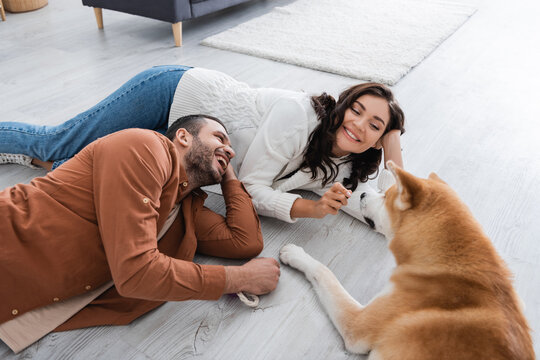 young couple laughing and lying of floor with akita inu dog.