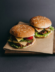 Delicious big juicy burger with tomatoes, cucumbers, cabbage, greens, cheese, cutlet on a gray background. Two sandwiches, fast food. Snack, appetizing, bun with sesame seeds. Serving in restaurant