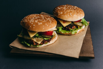 Delicious big juicy burger with tomatoes, cucumbers, cabbage, greens, cheese, cutlet on a gray background. Two sandwiches, fast food. Snack, appetizing, bun with sesame seeds. Serving in restaurant