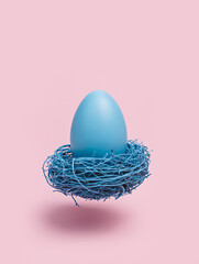 Blue colored egg and bird nest levitating and flying against pastel pink background. Minimal Easter...