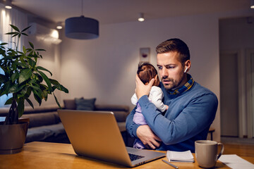 A busy father calming his baby girl and working online on the laptop from home.