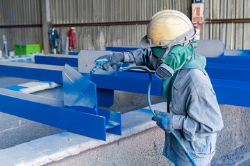 Painter is working to paint color topcoats on steel structures with a spray gun at the industrial factory, focusing on hand holding a spray gun.