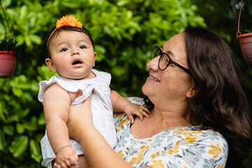 latina aunt smiling with her baby girl niece in her hands, outside - obrazy, fototapety, plakaty