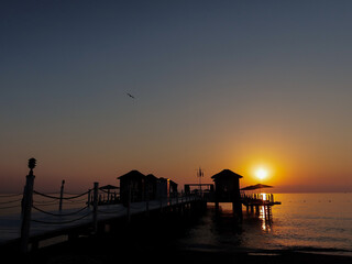 Naklejka na ściany i meble Amazing sunrise and bungalow silhouette and flying gull at the sea 