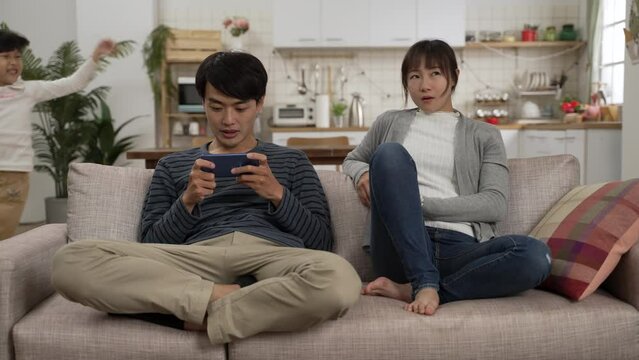 slow motion of addicted asian dad enjoying using smartphones and ignoring his annoyed wife and energetic daughter. the mother sighs while the girl is making noise at home