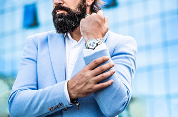 Businessman points to his watch on the background of the town. Man holds his watch. Portrait...