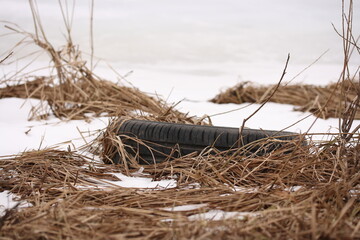 Car tire in the grass on the bank of a frozen river after snow melts