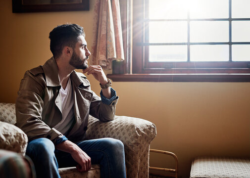 Thinking Things Through.... Shot Of A Handsome Young Man Deep In Thought While Sitting On A Chair At Home.