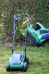 Fototapeta na wymiar A gardener attaching the grass basket of a electric lawn mower machine
