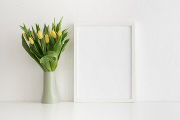 Bunch of tulips and empty frame on white table. Spring mockup. Easter background.