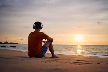 Rear view of man with headphones on beach. Serenity, contemplation and listening music at beautiful...
