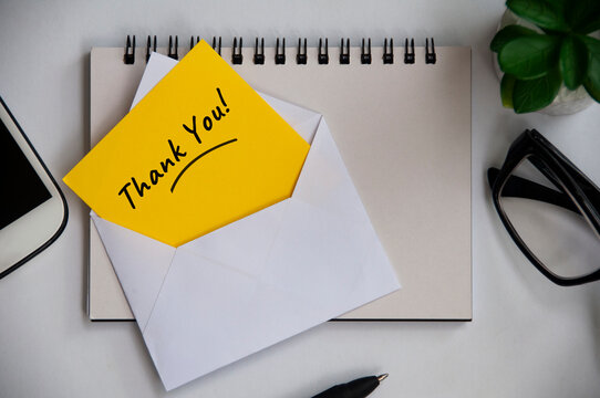 Thank you note on yellow paper in an envelope with office background concept.