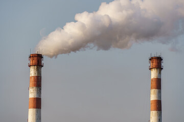 Clouds of smoke come out of factory chimneys against blue sky.