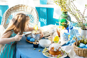 pretty little Armenian girl helps with baking for Easter on veranda on sunny spring day decorated with flowers and Easter decor, eggs, cake and willow branches, Easter family celebration