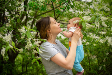 young mother walks with a newborn baby in a spring park among flowering trees - 495710290