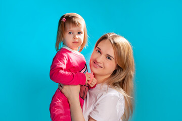 young mother and her little daughter in a pink dress on a blue background - 495710292
