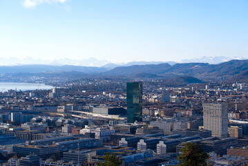 Fototapeta na wymiar Aerial view over City of Zürich with Prime Tower skyscraper and industrial area and mountains in the background on a blue and cloudy spring morning. Photo taken March 14th, 2022, Zurich, Switzerland.