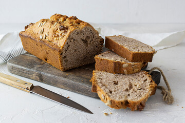Freshly baked bread with walnuts and seeds on a dark wooden plank. A knife on a bright table. Close-up. Light napkin in the background