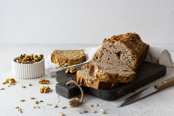 Fragrant bread with seeds and nuts on a dark board. Walnuts in a white vase in the background. Seeds are scattered on the table. Light background