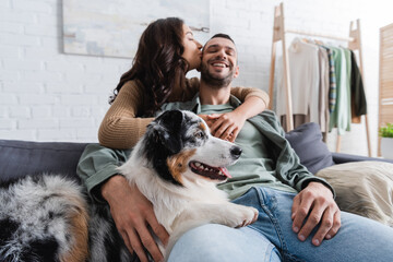 young woman kissing cheek of happy boyfriend near australian shepherd dog.