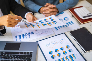 Two business people sit down to analyze financial data from earnings graphs showing the company's earnings to be presented at a meeting.