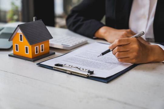 Real estate agent working sign agreement document contract for home loan insurance approving purchases for client with house model and key on table
