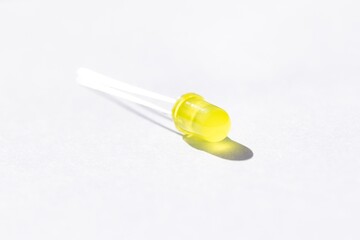 A studio portrait of a single yellow colored LED or color Light Emitting Diode lying on a white background, ready to be used in some kind of electronics PCB or circuit or print board.