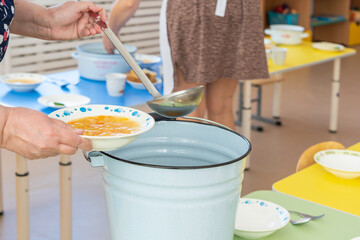 A kindergarten cook pours soup into a plate before lunch.