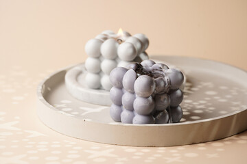 Two grey bubble candles on gray concrete tray on beige colored seamless surface with starry light shadows