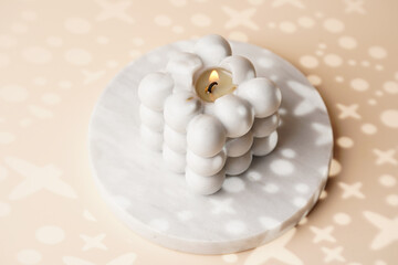 One grey bubble candle on marble tray on beige colored seamless surface with starry light shadows