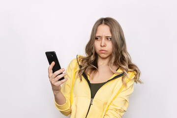 A frightened young caucasian blonde woman with wavy hair holds a mobile phone in her hand looking...