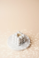 One grey bubble candle on marble tray on beige colored seamless surface with starry light shadows