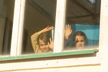 Little children with a sad look. Sad kids by the window. A child cries in the window of an old house