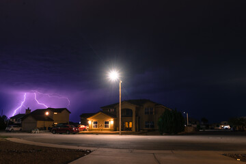 View of the street and the house against the violet lightning in the sky.