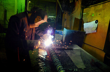 A welder in a protective suit and mask cuts a metal pipe by welding
